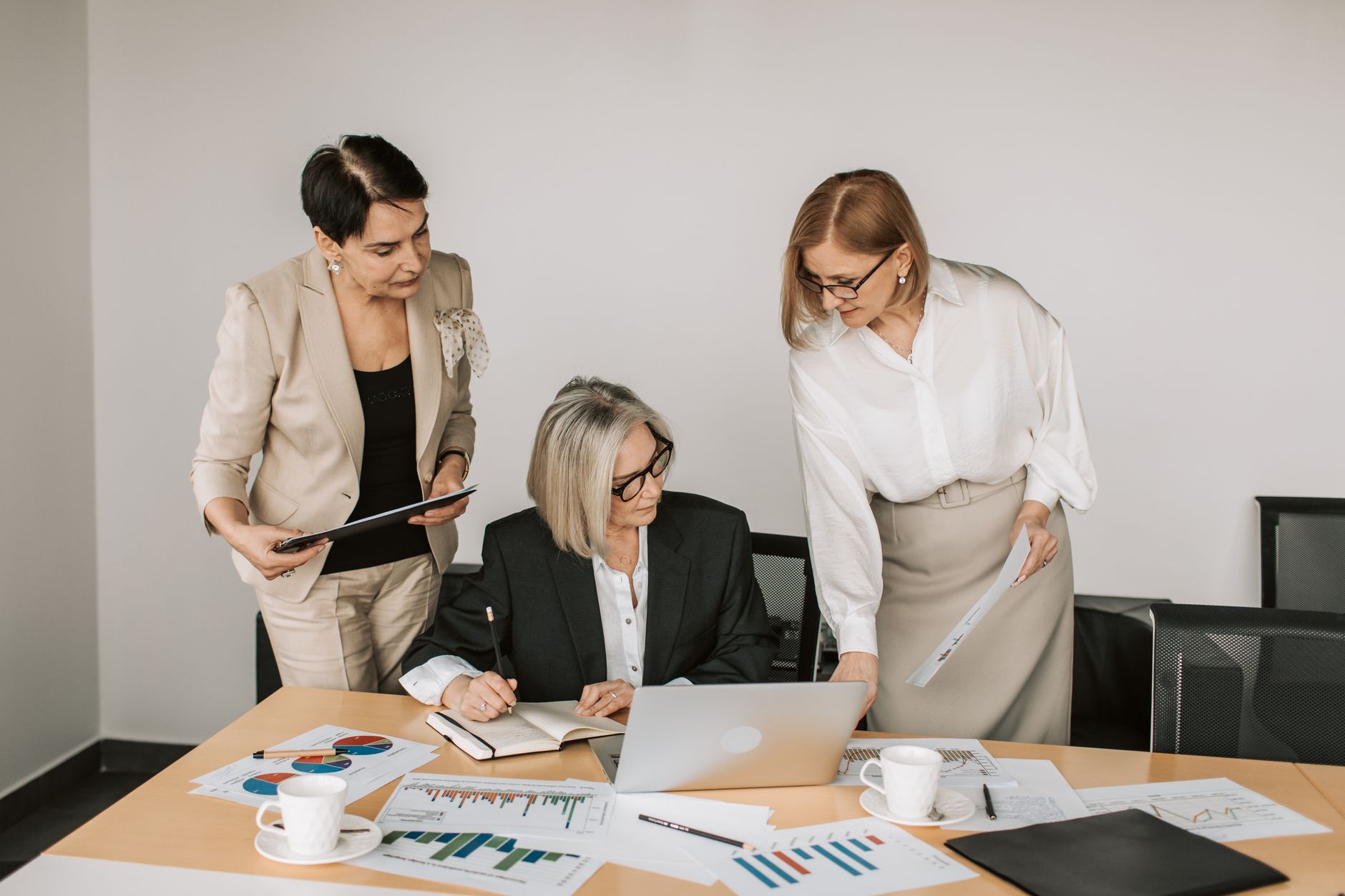 Three businesswomen discussing documents during a meeting in a modern office setting. — NOTICES IN CHOOSING THE PERFECT FOREX